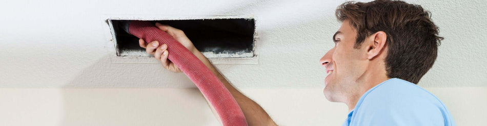 Professional cleaning of air ducts using flexible hose for effective suction and maneuverability in HVAC systems.