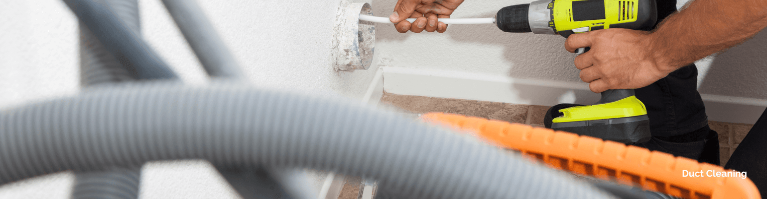 Person using a drill for duct cleaning with hoses in the foreground, showcasing residential duct maintenance.