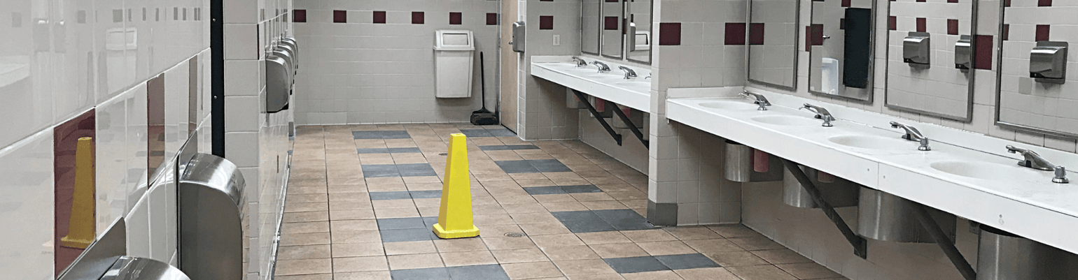 Clean commercial restroom with sinks, mirrors, and wet floor caution sign, highlighting janitorial efficiency.