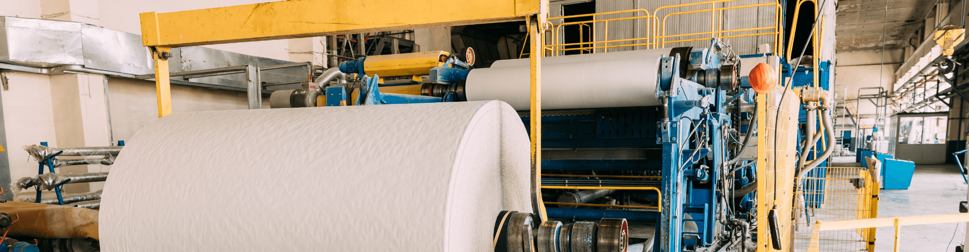 Paper mill machinery with large rolls of paper for high-speed production and material flow.
