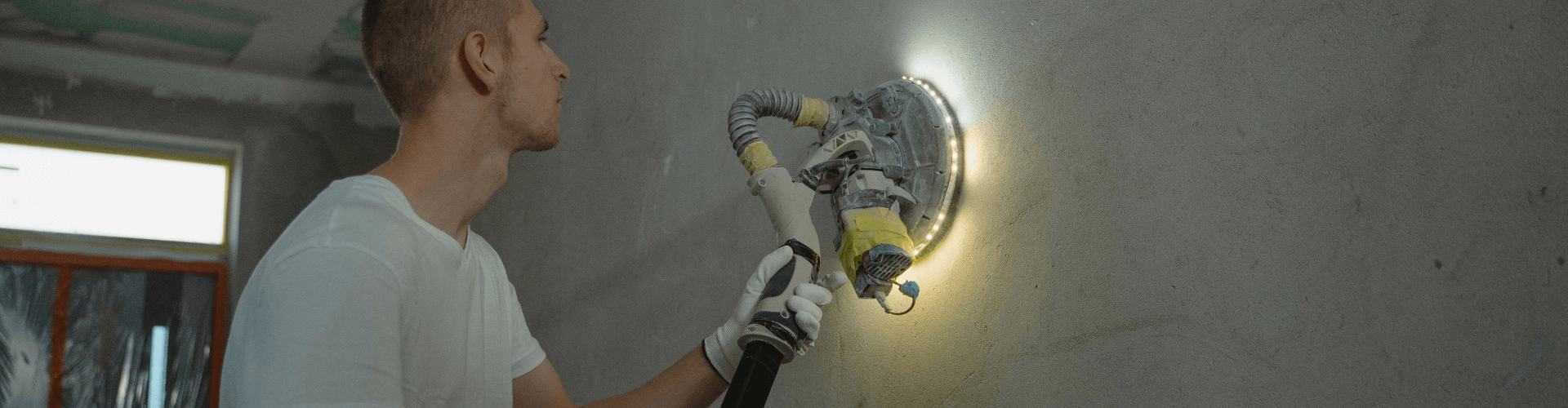 Man using a wall sander with dust extraction to maintain clean air during drywall finishing.