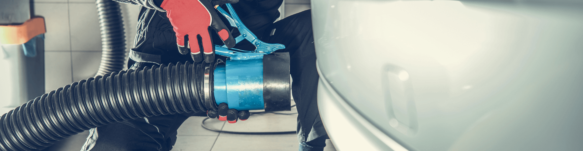 Technician connecting a vehicle exhaust hose for efficient gas extraction in a garage environment.