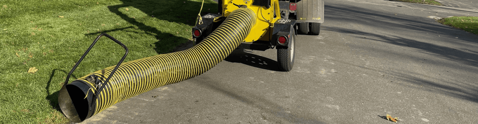 Commercial lawn and leaf vacuum hose efficiently collecting yard debris on a residential street.