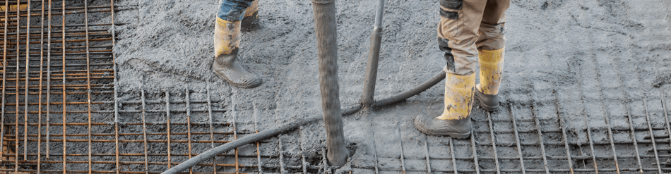 Workers in rubber boots pouring concrete into rebar grid for construction, demonstrating wet concrete transfer system.