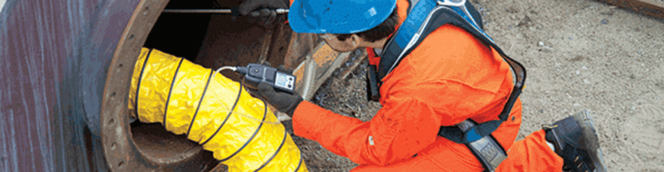 Worker in safety gear inspecting yellow ventilation duct in confined space for fresh air deployment.