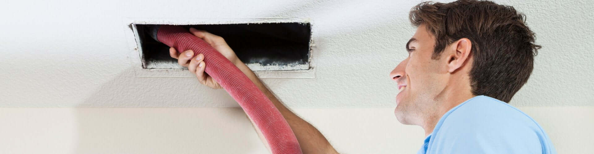Professional cleaning of air ducts using flexible hose for effective suction and maneuverability in HVAC systems.