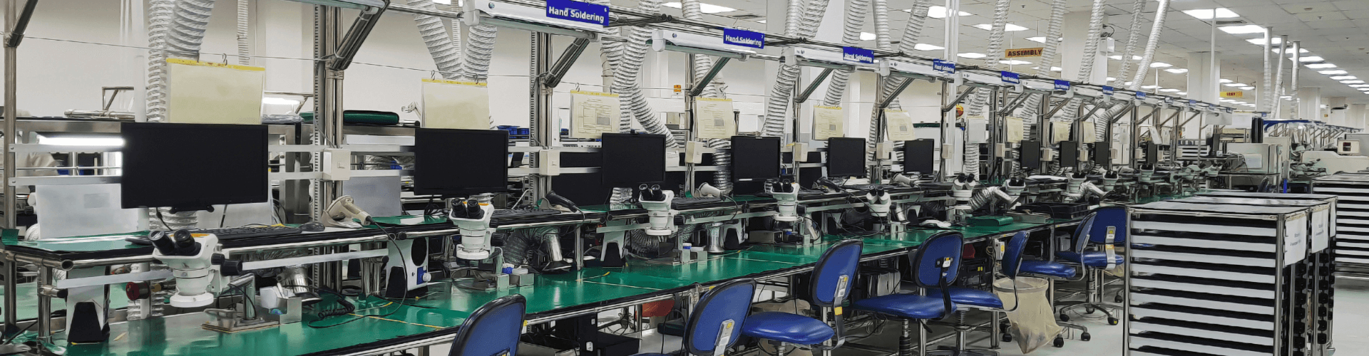Circuit board manufacturing workspace with precision airflow systems, benches, and monitors for electronics assembly.