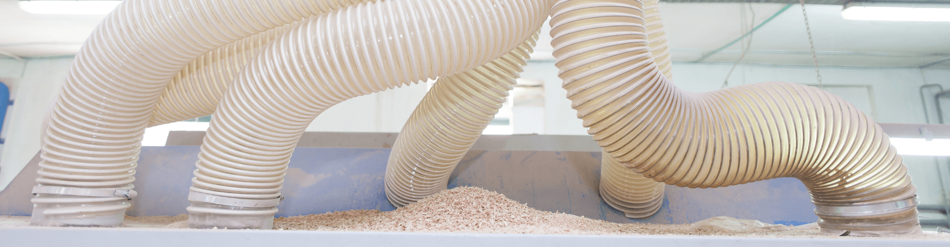 Heavy-duty dust collection hoses directing debris into a vacuum system in an industrial workshop.
