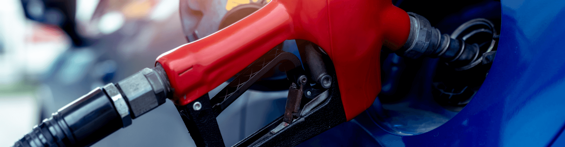 Close-up of a red gasoline pump nozzle inserted into a vehicle, capturing gasoline vapors during fueling.