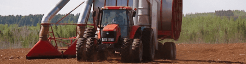 Tractor equipped with peat moss vacuum, efficiently moving peat moss in a lush, green field.