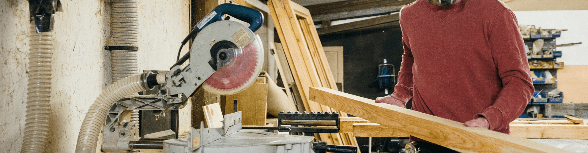 Person using a miter saw in a workshop with dust collection system for residential woodworking projects.