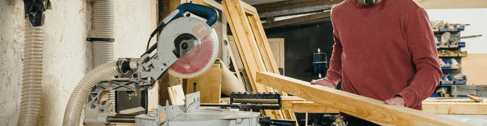 Person using a miter saw in a workshop with dust collection system for residential woodworking projects.