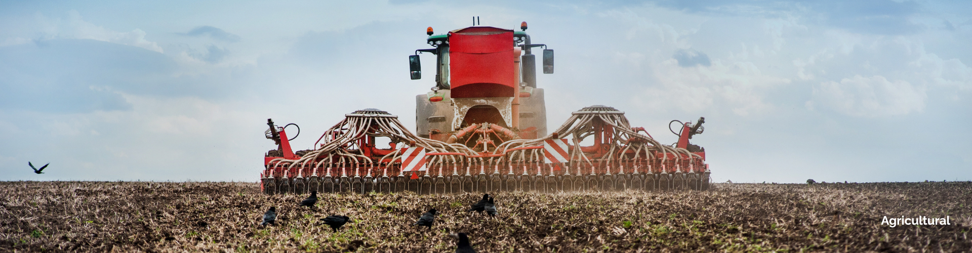 rear view of a agricultural tractor pulling a seeder in a field with a clear sky in the background