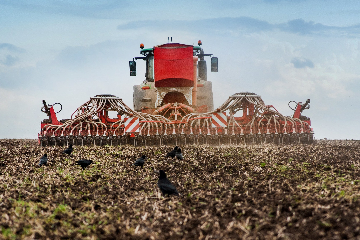 Red agricultural seeder machine seeding a field with a clear sky in the background