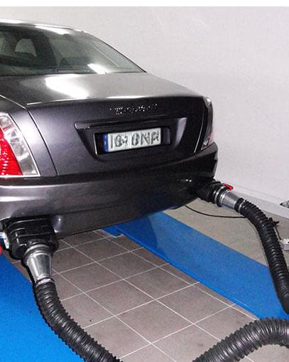 Car being serviced with hoses connected to it on a tiled floor.
