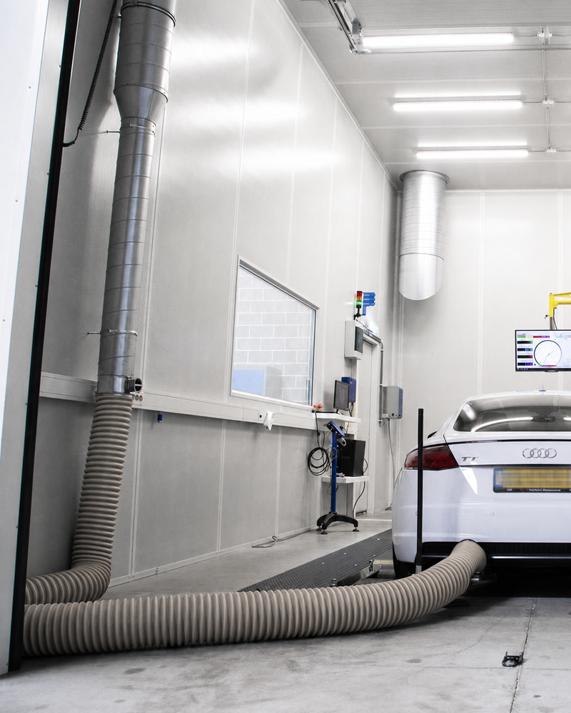 Car in a white paint booth with exhaust ducts and equipment in a garage setting.