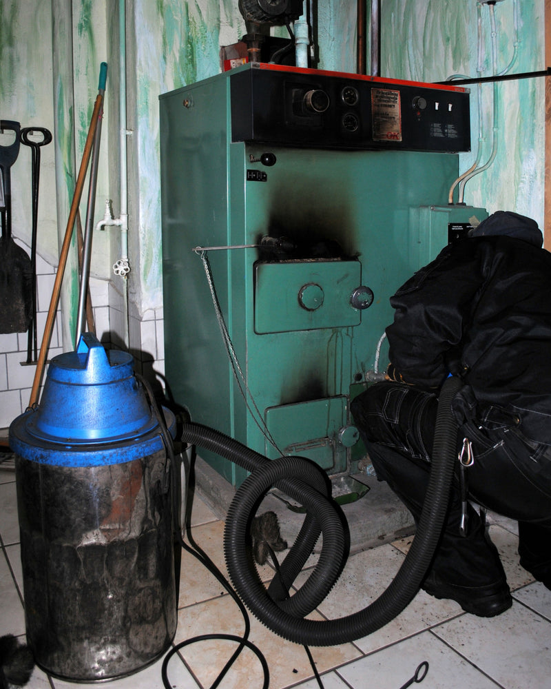 Person using a vacuum cleaner next to a green industrial machine in a room with tiled walls.