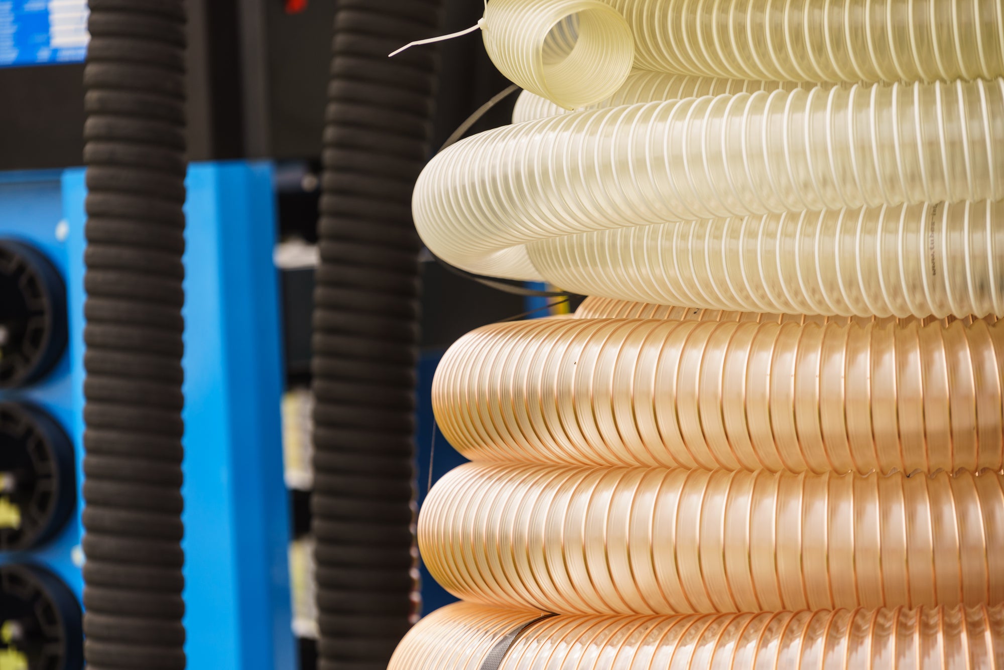 Stack of beige flexible hoses with a blue industrial machine in the background