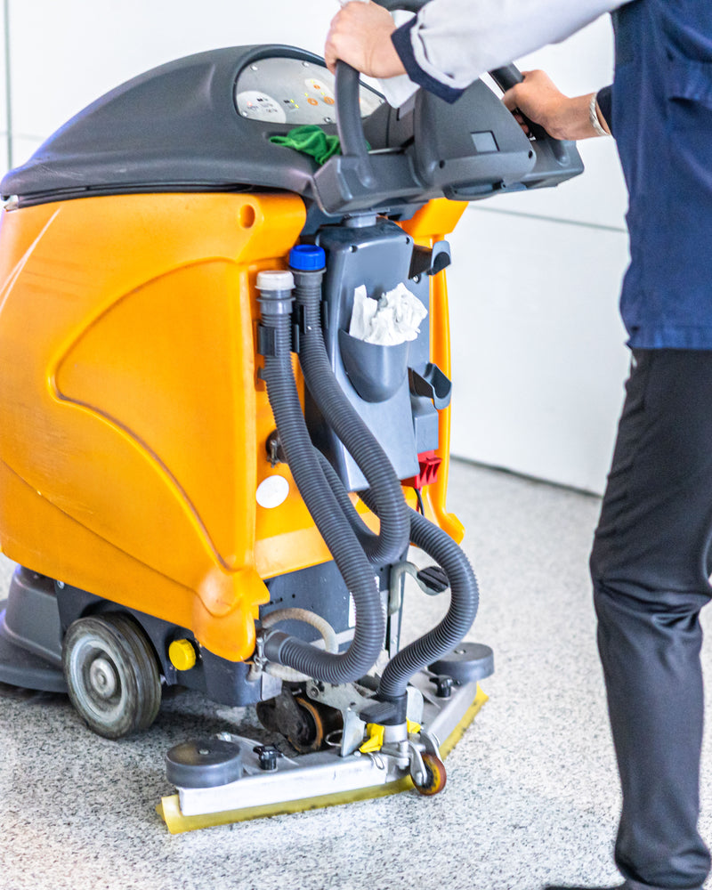 Person operating a yellow floor cleaning machine on a concrete floor.