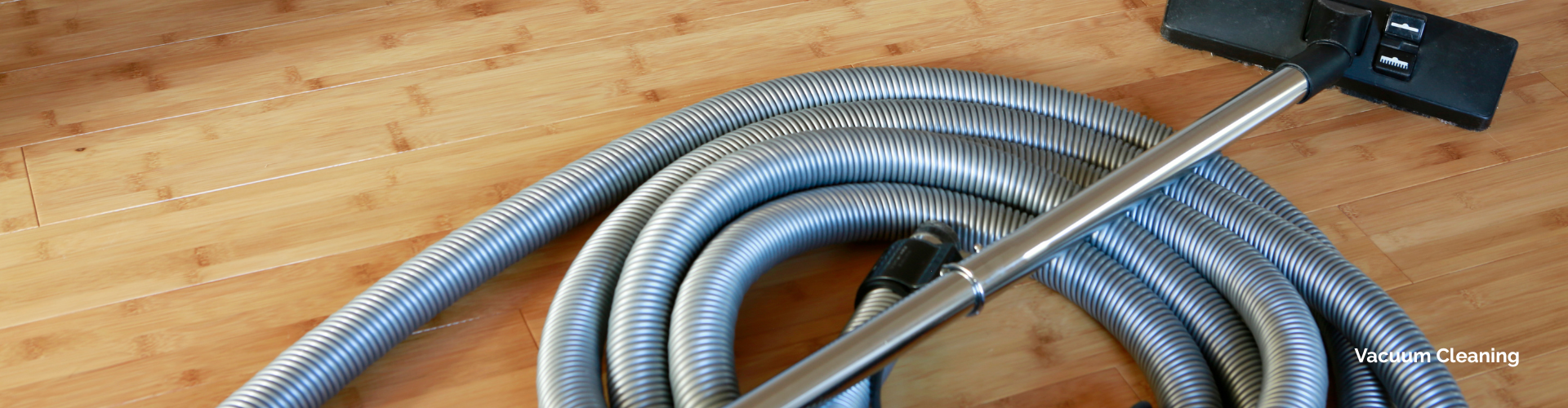 Coiled commercial vacuum hose with a floor cleaning wand on a hardwood floor