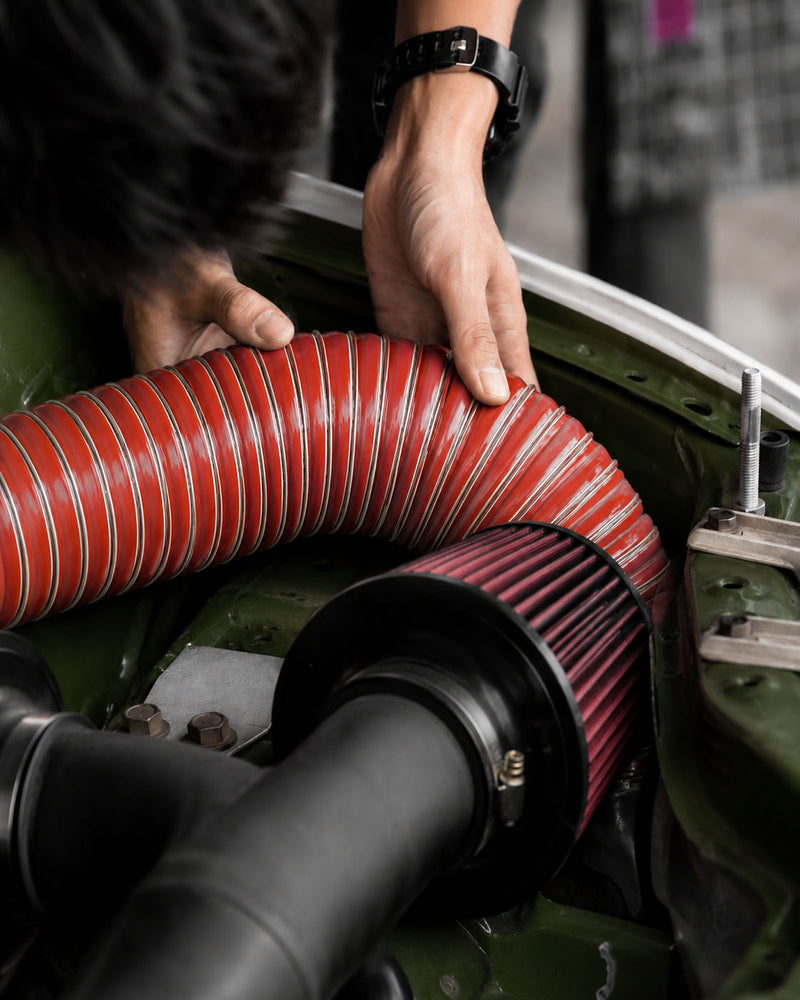 Person using a red hose on a vehicle engine
